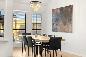 A dining area with a wooden table, black chairs, a chandelier, and a large abstract painting on the wall. - Heart of Grand Prairie 3BD With Pool, Patio, BBQ (Grand Prairie)