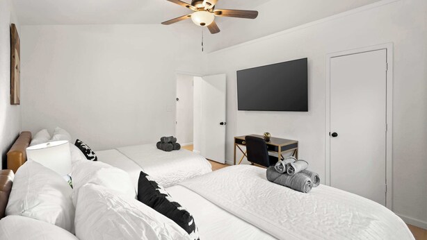 A modern hotel room with a ceiling fan, two beds, a desk, a TV, and a wardrobe. - Heart of Grand Prairie 3BD With Pool, Patio, BBQ (Grand Prairie)