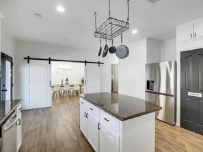 A modern kitchen with a central island, stainless steel appliances, and a hanging pot rack. - The Best of DFW - Pool, Hot Tub, Cinema Room (Fort Worth)