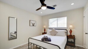 A bedroom with a bed, two bedside lamps, a ceiling fan, a window, and a mirror. - Highland Village - 4BR w Backyard Pool Oasis (Lewisville)