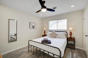 A bedroom with a bed, two bedside lamps, a ceiling fan, a window, and a mirror. - Highland Village - 4BR w Backyard Pool Oasis (Lewisville)