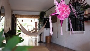 Una habitación con una hamaca, un adorno rosa, una cesta de mimbre y una ventana con reja de metal.
