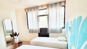 Una habitación con dos camas, un ventilador de techo, una ventana con cortinas, un espejo y una pared con estampado floral.