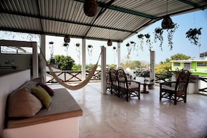 A covered outdoor seating area with a hammock, wicker chairs, and hanging planters.