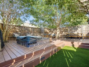 Un jardin avec un jacuzzi, une terrasse en bois et une pelouse.