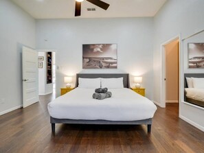 Une chambre à coucher avec un lit, des lampes de chevet, un ventilateur de plafond, une porte et un tableau encadré au mur.