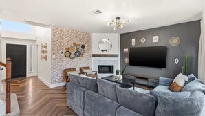Ein modernes Wohnzimmer mit Ziegelwand, Kamin, großem Fernseher und einer gemütlichen Sitzecke.