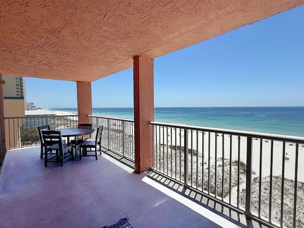Ein Balkon mit Tisch und Stühlen, der auf einen Strand mit freiem Blick auf das Meer und entfernte Gebäude blickt.