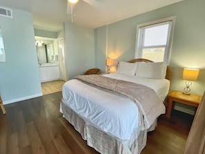 Ein Schlafzimmer mit Bett, Nachttischlampen, einem Nachttisch, einem Spiegel und einem Badezimmer mit Dusche und Toilette.