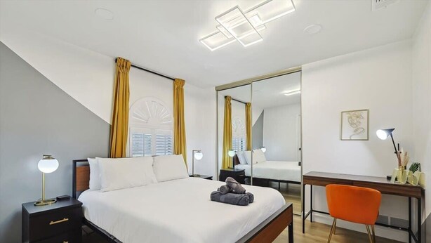A modern hotel room with a large bed, bedside tables with lamps, a desk with a chair, and a large mirror. - Plano Perfect Getaway - Pool, Hot Tub, BBQ Grill (Plano)