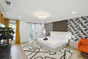 A modern bedroom with a bed, a nightstand, a plant, and a view of the outdoors. - Plano Perfect Getaway - Pool, Hot Tub, BBQ Grill (Plano)