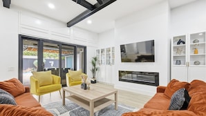 A modern living room with orange sofas, a yellow armchair, a wooden coffee table, and a fireplace. - Plano Perfect Getaway - Pool, Hot Tub, BBQ Grill (Plano)
