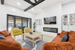 Ein modernes Wohnzimmer mit Kamin, Fernseher und großem Fenster mit Blick auf einen Garten.