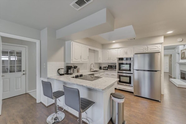 A modern kitchen with white cabinets, a stainless steel refrigerator, a built-in oven, and a large island with bar stools. - Spacious and Modern Home With Private Pool (Plano)