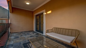 En balkon med en fletstol, et glasbord og en loftlampe. Der er en dør med glasfelter.