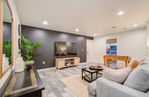 Uma sala de estar moderna com televisão de tela plana, um sofá, uma mesa de centro e uma mesa de pebolim.
