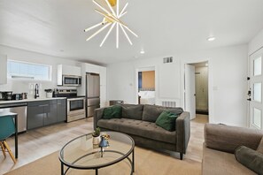 Ein modernes Wohnzimmer mit einer Couch, einem Glastisch und einer Küchenzeile mit Geräten.