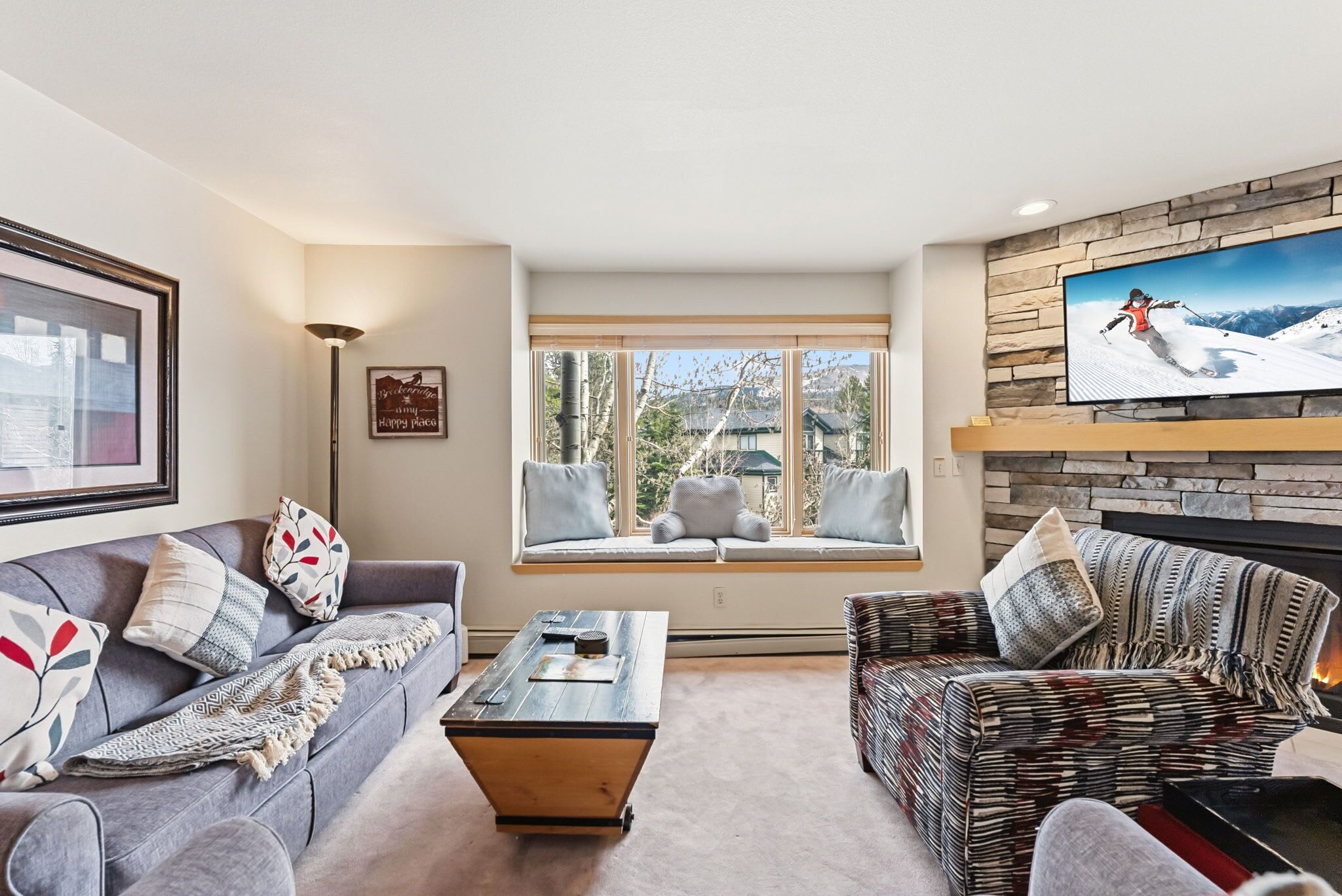 A living room with a sofa, a patterned armchair, a coffee table, a fireplace, and a large TV.
