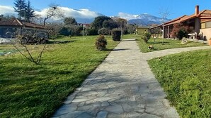 A stone pathway leading through a grassy area with buildings on either side, a mountain in the background, and a clear sky.
