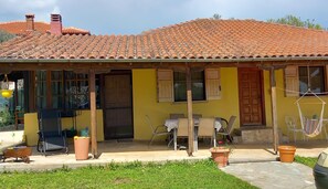 A yellow building with a tiled roof, a wooden door, and a table with chairs outside.
