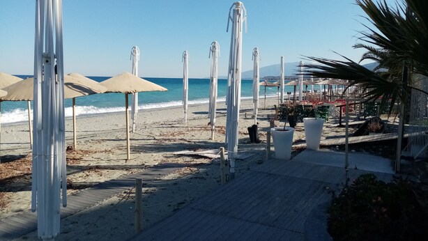 A beach with umbrellas, a wooden walkway, and a view of the sea.