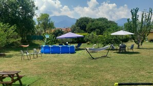A grassy outdoor area with a pool, lounge chairs, umbrellas, and a hammock.
