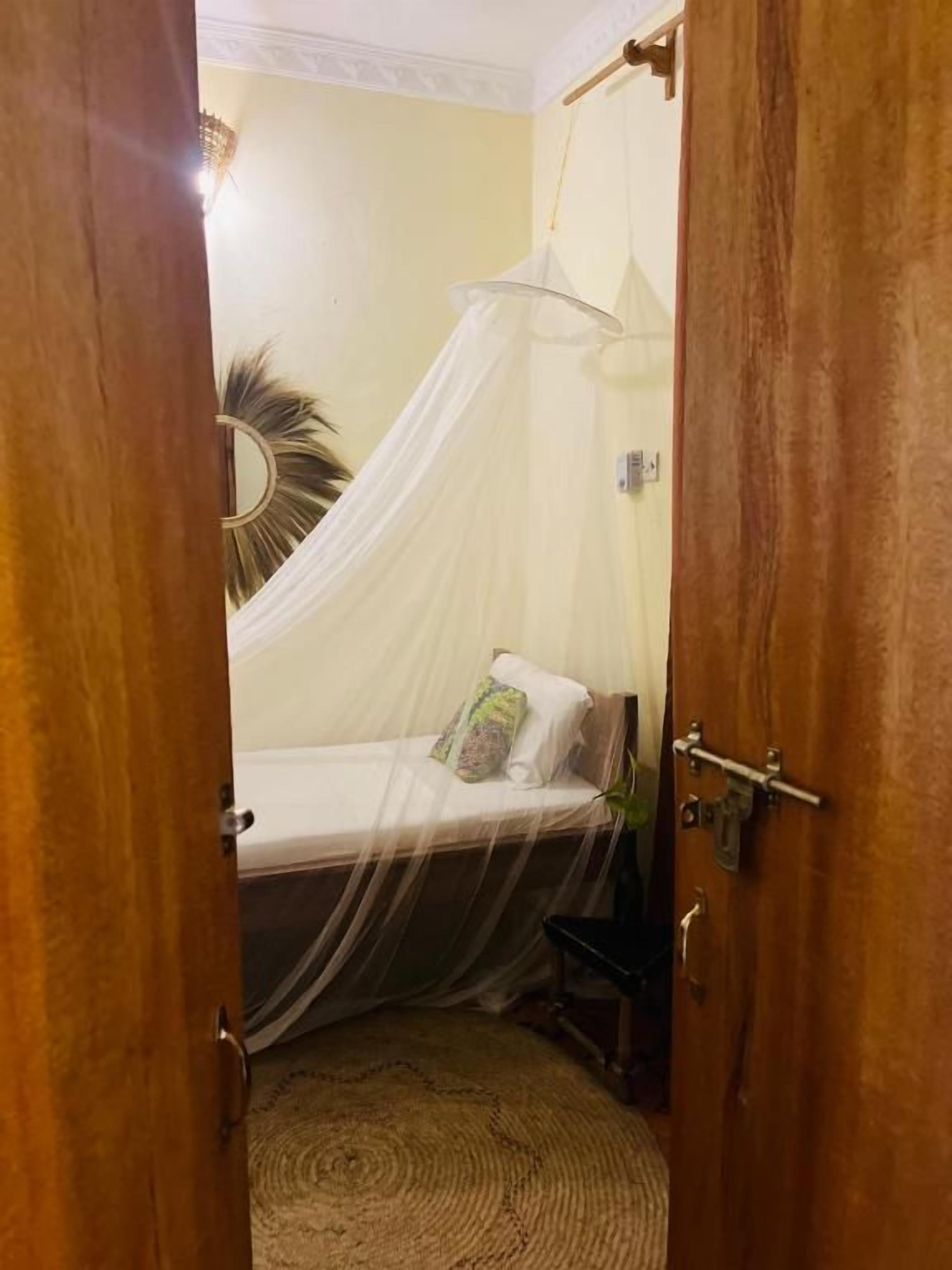 A room with a bed under a white canopy, a round mirror on the wall, and a wooden door.
