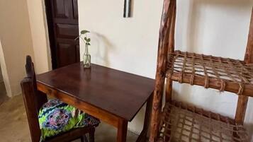 Une table à manger en bois, accompagnée d’une chaise, d’une étagère en osier et d’une porte visible au fond.
