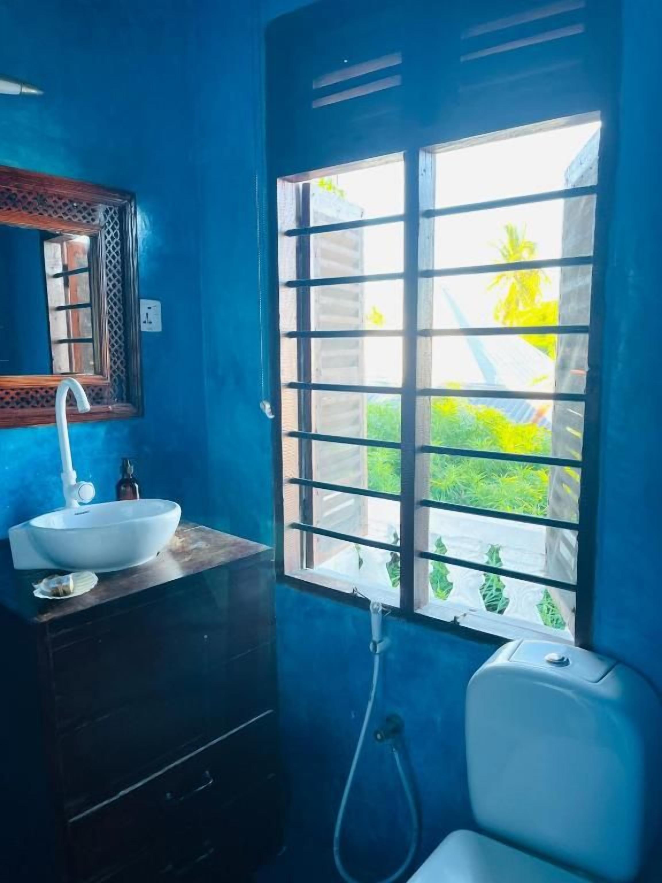 A bathroom with a white sink, dark wooden cabinet, and a window with a view of greenery.