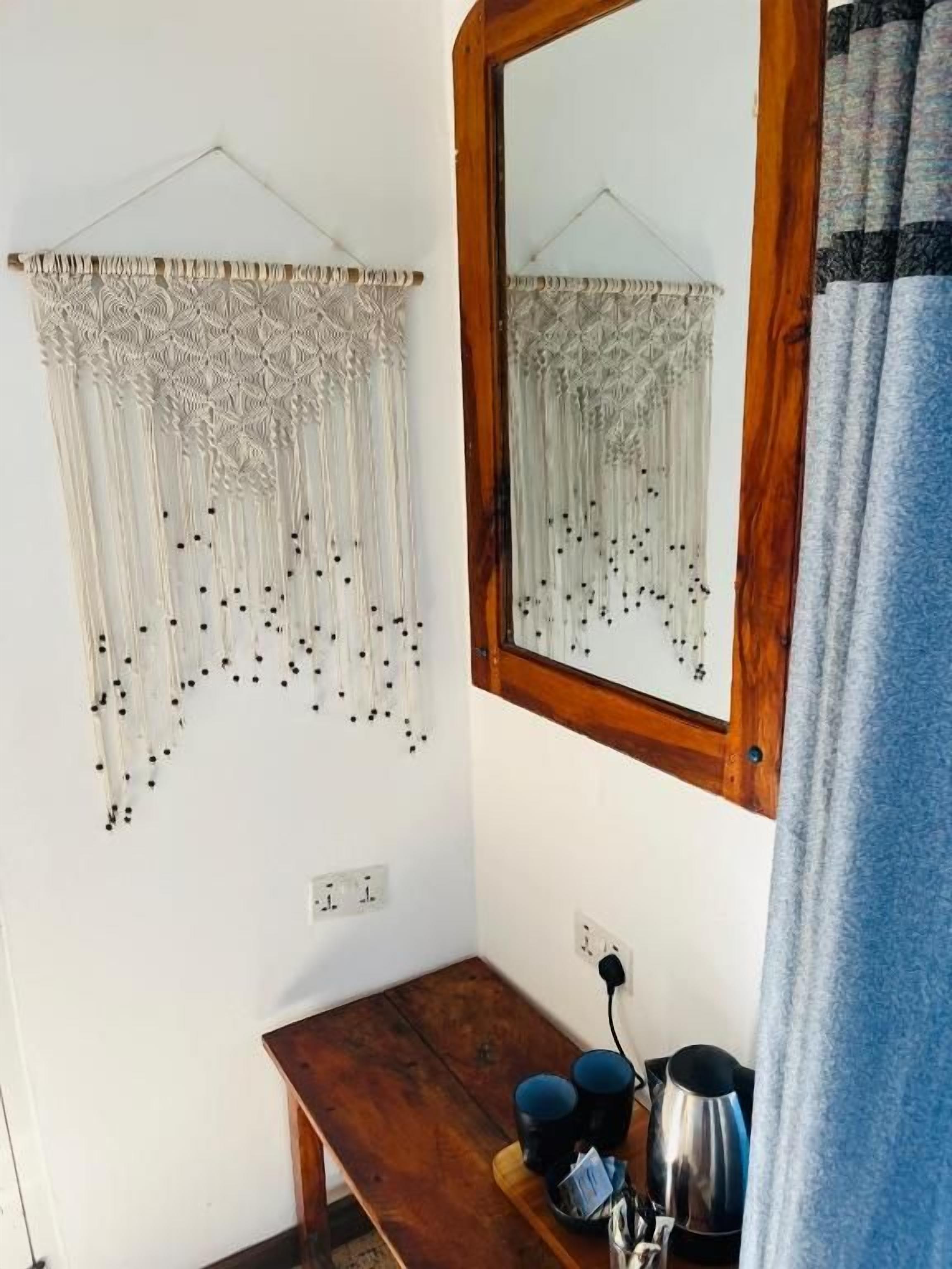 A room with a macrame wall hanging, a wooden table with a kettle, and a mirror with a wooden frame.