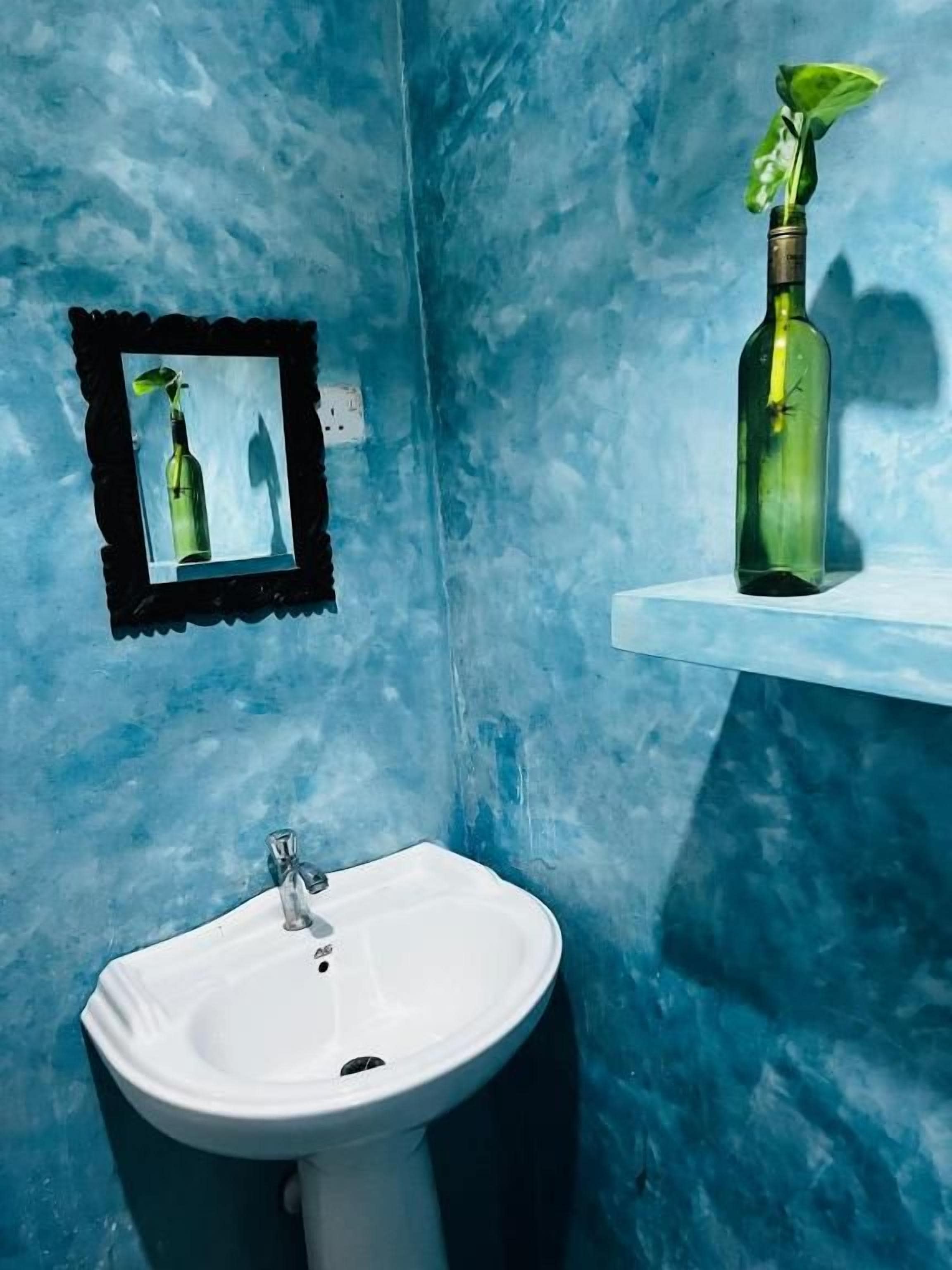 A bathroom with a white sink, a framed mirror, and a green bottle on a shelf.