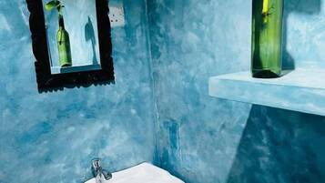 A bathroom with a white sink, a framed mirror, and a green bottle on a shelf.