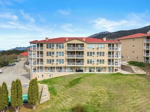 A multi-story hotel with balconies, a parking lot, and a mountainous backdrop.