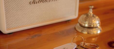 A wooden table with a white speaker labeled 'Marshall,' a silver bell, and a keychain with 'The Mossetide Hotel' on it.