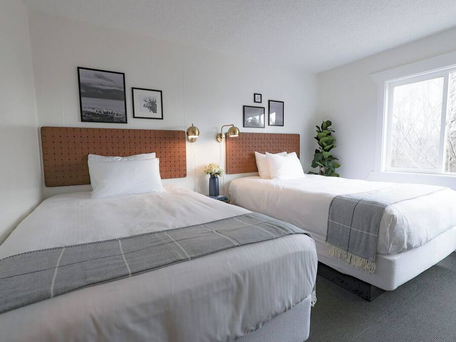 Ein Hotelzimmer mit zwei Betten, einem großen Fenster und gerahmten Bildern an der Wand.