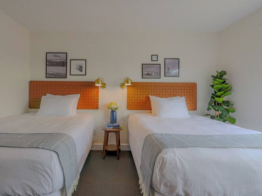 Hotellihuone, jossa on kaksi sänkyä, pieni pöytä maljakolla ja seinällä on kehystettyjä kuvia.