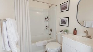 A bathroom with a shower, toilet, vanity, and two framed pictures on the wall.