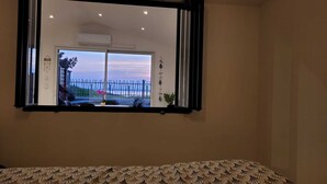 Een kamer met een groot raam, een bed met beddengoed met een patroon en een luchtverkoeler aan de muur.