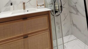 Een moderne badkamer met een douche met glazen wand, een ronde spiegel en een houten wastafelmeubel.