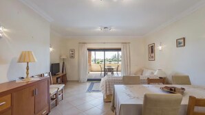 Una habitación de hotel con cama, escritorio, televisor, sofá y balcón con mesa y sillas.