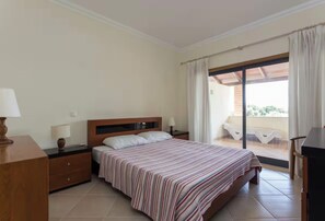 A hotel room with a bed, bedside tables, a lamp, a window with curtains, and a view of the outside. - Apartamento moderno com piscina em Vilamoura (Quarteira)