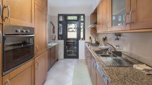 Una cocina con armarios de madera, electrodomésticos de acero inoxidable, encimera de granito y vistas a través de un ventanal.