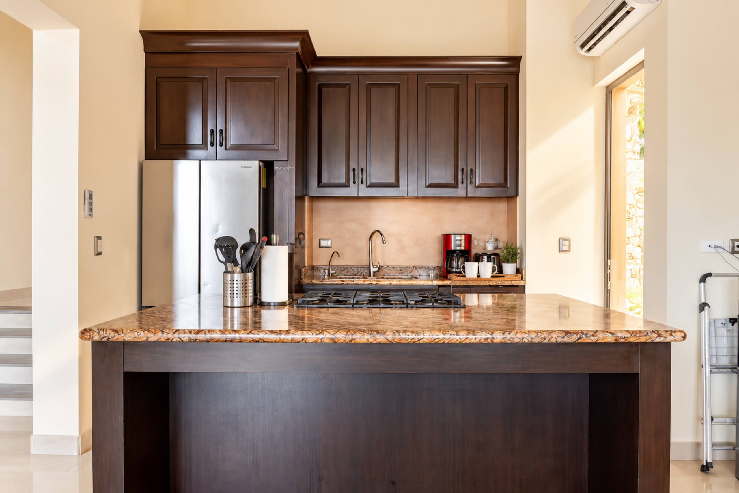 A kitchen with dark wood cabinets, a stainless steel refrigerator, a granite countertop, a gas stove, and a coffee maker.