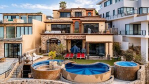 A modern multi-story house with a swimming pool, outdoor seating, and a stone facade.