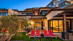A modern house with a swimming pool, red lounge chairs, and a well-maintained garden.