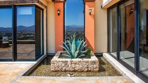 A modern building with large glass doors, a stone planter with a plant, and a clear view of a distant cityscape.