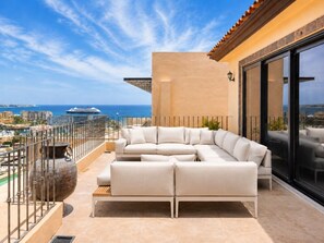 Ein Balkon mit einem weißen Ecksofa, einem großen Zierteich und Blick auf das Meer sowie die Stadtlandschaft.