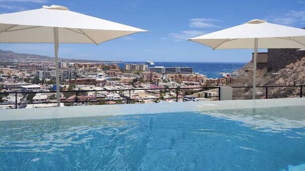 A pool with a city view, two umbrellas, and a clear sky. - Ocean View-Heated Pool-Walk everywhere in Cabo (Cabo San Lucas)