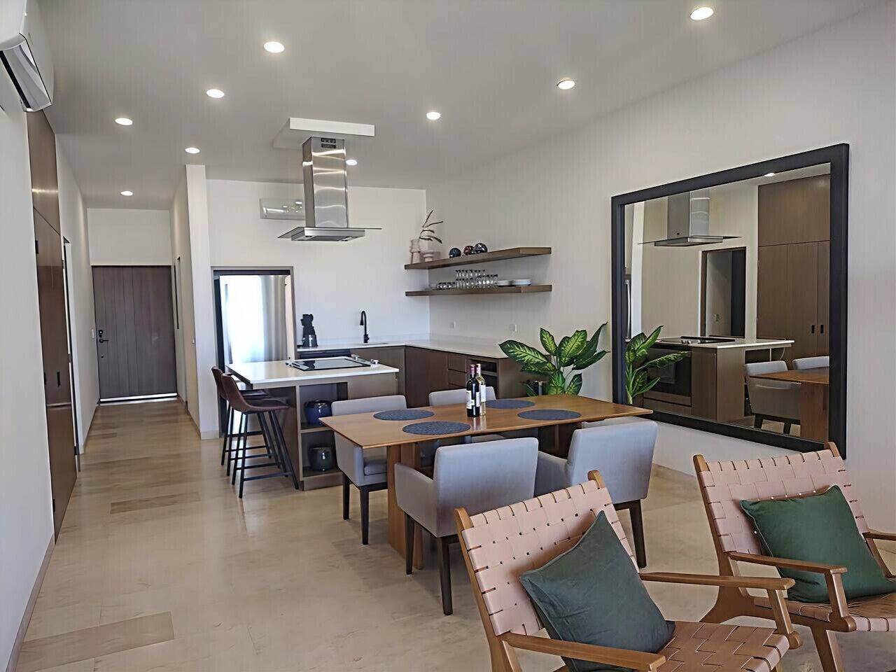 A modern kitchen with built-in appliances, a dining area with a wooden table and chairs, and a large mirror on the wall.