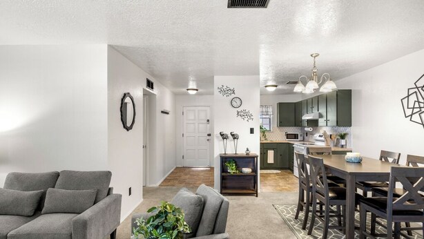 A modern living room with a grey sofa, a dining area with a wooden table and chairs, and a kitchen in the background.
